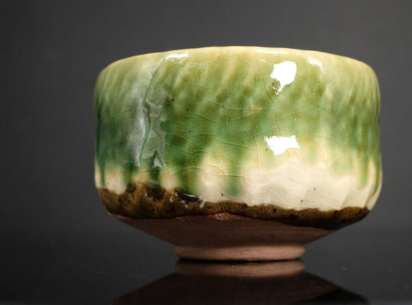 Green ceramic bowl on a reflective surface with a dark background