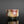 Load image into Gallery viewer, A handmade ceramic sake cup with a rustic, hand-painted glaze featuring mottled red, brown, beige, and green colors, set against a dark gray background with a reflective black surface below.
