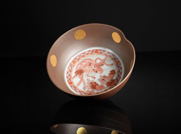 A ceramic bowl with a warm brown exterior, decorated with gold circular accents on the side and a white interior featuring a red and orange floral pattern, set against a solid black background.