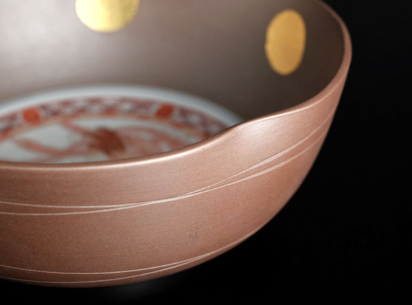 Close-up of a metallic bronze-colored bowl with gold circular accents on the interior, set against a solid black background.
