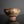 將圖片載入到圖庫檢視器中， An ancient-looking rustic clay bowl with a textured, weathered surface in earthy brown, beige, and gray tones, set against a dark gray background with a reflective black surface below.

