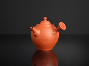 Terracotta teapot on a reflective black surface with a dark background