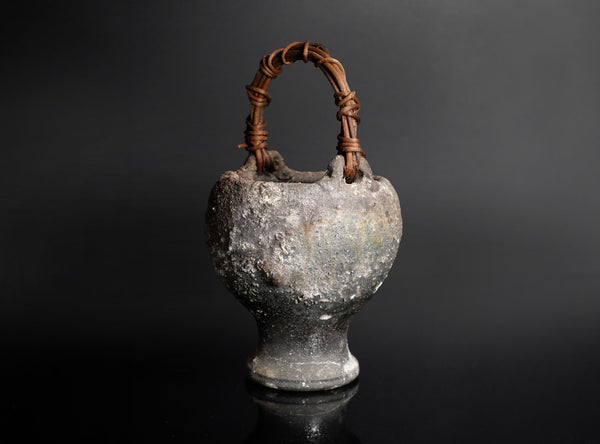 Vintage ceramic vase with a woven handle on a black background