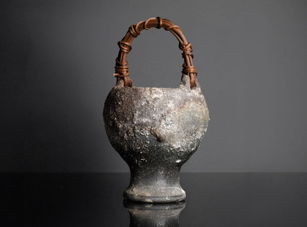Vintage ceramic vase with a woven handle on a black background