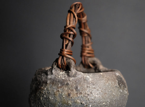 Vintage ceramic vase with a woven handle on a black background