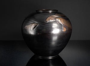 Black ceramic vase with fish designs on a dark background