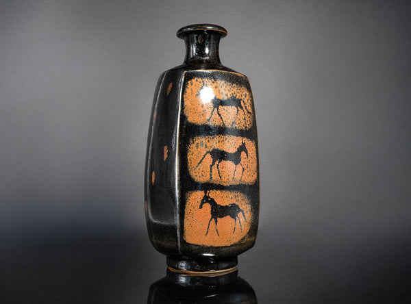 Black ceramic vase with orange designs of horses on a gray background