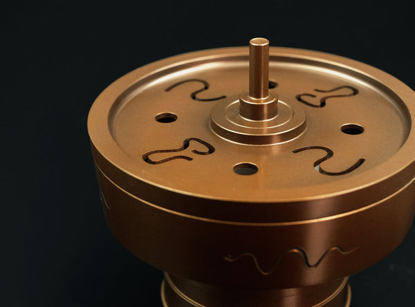 Bronze-colored metal object with engraved patterns on a black background