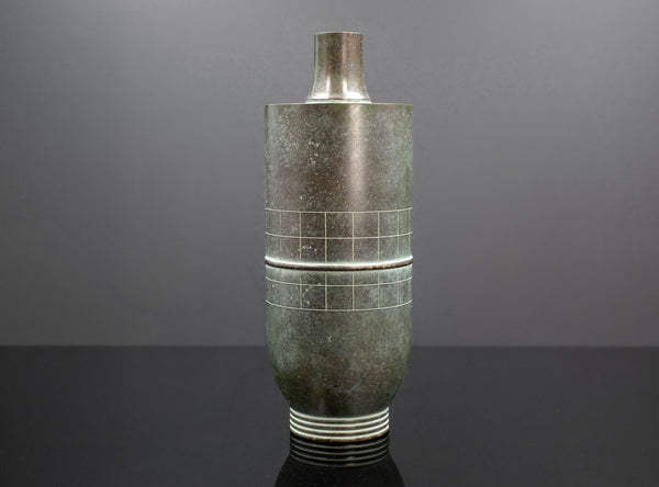 Tall cylindrical vase with textured surface and grid pattern on a gray background