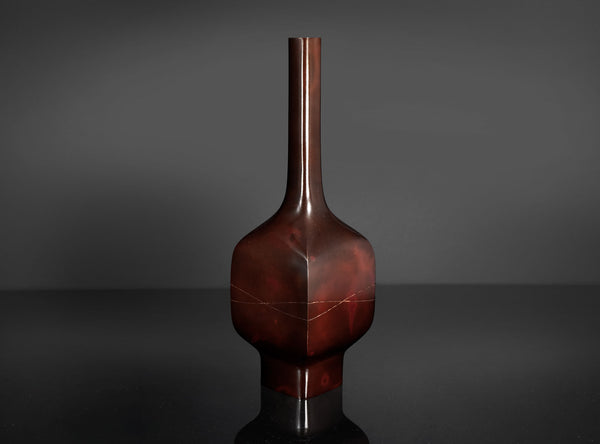 A glossy dark reddish-brown ceramic vase with a narrow neck and bulbous body, standing on a reflective black surface against a dark gray background.