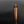 Load image into Gallery viewer, A metallic copper-colored cylindrical container or grinder with horizontal grooved details, standing upright on a reflective black surface against a dark gray gradient background.
