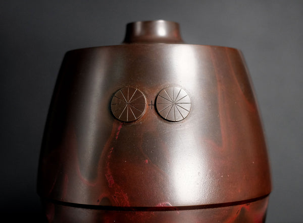 A metallic reddish-brown urn-shaped vase, photographed against a dark gray to black gradient studio background.