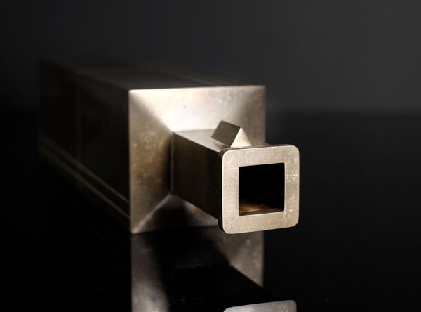 A rectangular metallic box with a textured, brushed silver finish and a small rectangular window on top, set against a dark gray gradient background.