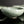 Load image into Gallery viewer, A close-up of a glossy pale green ceramic bowl with a crackle glaze pattern, shown with other matching bowls blurred in the background on a dark reflective surface.
