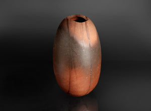 A small organic-shaped ceramic vase with a wide opening, featuring a mottled finish that transitions from dark brown to warm terracotta orange, set against a dark gradient background.