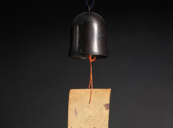 Black bell hanging from a string on a dark background