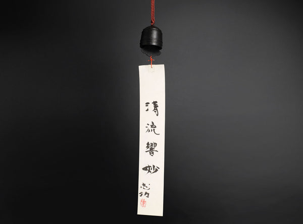 A finely crafted sahari wind bell, A hanging calligraphy brush with a black ink stick, red cord, and long white paper brush stroke featuring black calligraphy characters, set against a dark gray background.