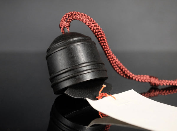 A finely crafted sahari wind bell, A hanging calligraphy brush with a black ink stick, red cord, and long white paper brush stroke featuring black calligraphy characters, set against a dark gray background.