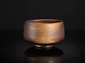 Brown ceramic bowl on a black reflective surface with a dark background