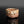 Load image into Gallery viewer, A rustic, handcrafted ceramic cup with a rough, textured surface resembling natural stone, featuring earthy brown, beige, and reddish tones, set against a dark reflective background
