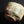 Load image into Gallery viewer, A handmade ceramic bowl with a rough, organic shape and a textured glaze featuring green, beige, and brown tones, photographed on a reflective black surface.
