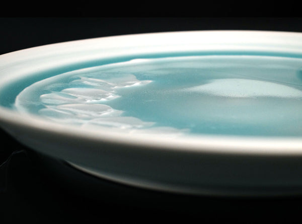 Close-up of a ceramic plate with a light blue interior glaze on a black background