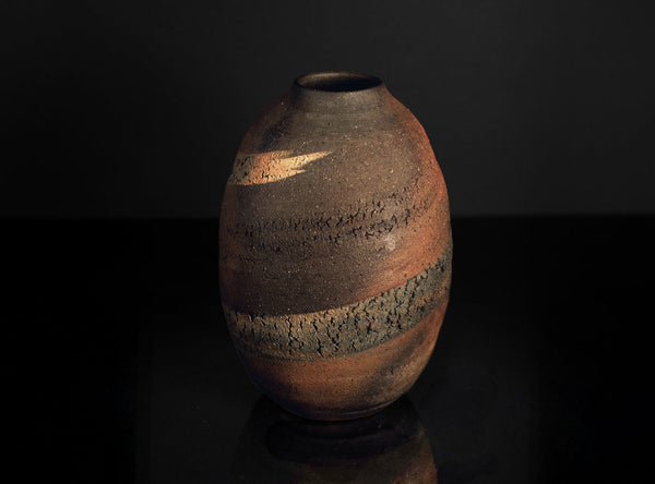 Textured ceramic vase on a dark reflective surface with a black background