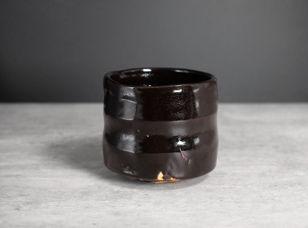 A dark brown glossy ceramic cup with a textured, wavy horizontal design, set against a neutral gray background.