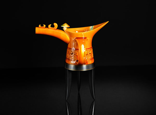 Orange ceramic teapot with decorative patterns on a black background
