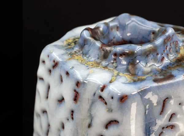 Close-up of a ceramic vase with textured surface and decorative patterns on a black background