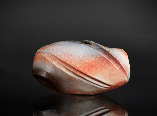 Ceramic vase with a textured surface on a reflective black surface