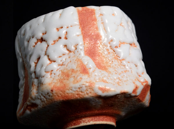 Close-up of a ceramic piece with white glaze and orange-brown speckles on a black background