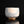Load image into Gallery viewer, A handmade ceramic tea bowl with a textured, speckled glaze in off-white and light blue, standing on a reflective black surface against a solid black background.
