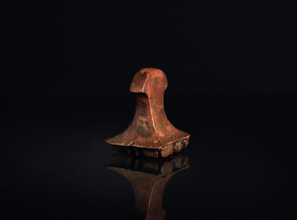 A square bronze seal stamp with red-orange engraved characters, displayed on a reflective black surface against a dark background.