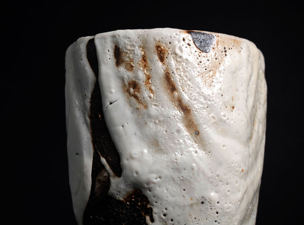 Close-up of a textured ceramic or stone object with brown and black markings on a black background