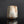 Load image into Gallery viewer, A rustic, handcrafted ceramic cup with a textured, weathered finish in earthy beige, brown, and light blue glazes, standing on a reflective black surface against a dark gray background.
