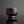 Load image into Gallery viewer, A small handmade ceramic cup with a textured, rustic finish in dark brown and black tones, set against a dark gray background with a soft reflection below.
