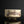 Load image into Gallery viewer, A handmade ceramic tea bowl with a textured off-white glaze and dark brown painted brushstrokes, set against a dark black background with a soft reflection below.

