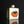 Load image into Gallery viewer, A square ceramic bottle with a white face, green side glaze, and a stylized orange and blue graphic on the front, set against a dark reflective background.
