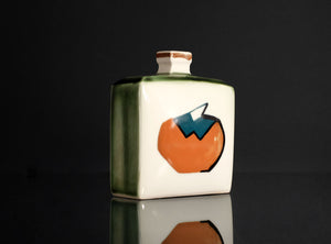 A square ceramic bottle with a white face, green side glaze, and a stylized orange and blue graphic on the front, set against a dark reflective background.