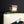 Load image into Gallery viewer, Close-up of a glossy ceramic bottle or vase with a white body, dark green band, and abstract blue, orange, and black painted details near the bottom, set against a dark gray background.
