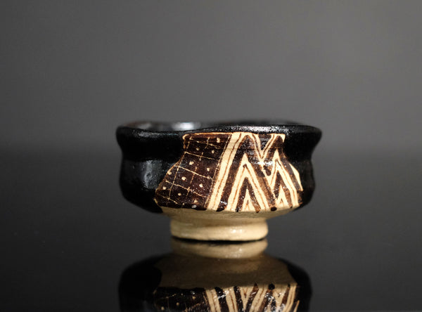 Ceramic cup with black and beige geometric pattern on a reflective surface with dark background
