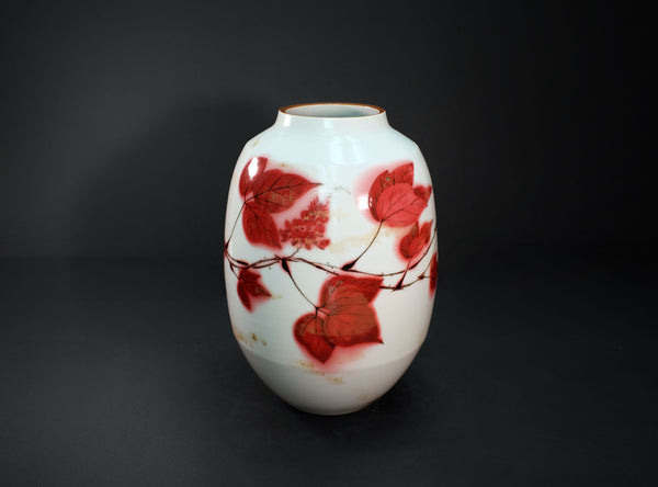 A white ceramic vase decorated with red painted leaves and berries, set against a dark black background.