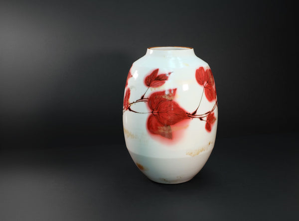 A white ceramic vase decorated with red cherry blossoms and brown branches, set against a dark gray background.