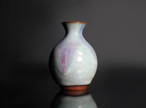 Ceramic sake bottle with a glossy finish on a reflective surface against a dark background