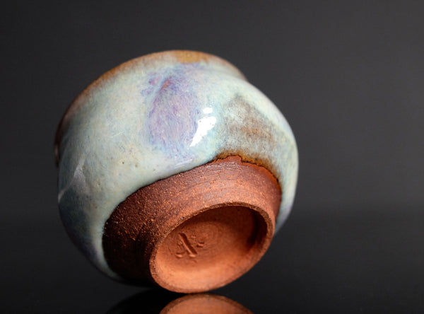 Ceramic sake cup with multicolored glaze on a dark background