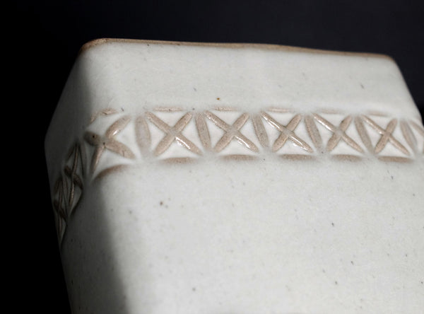 Close-up of a white ceramic vase with decorative lattice pattern on a black background