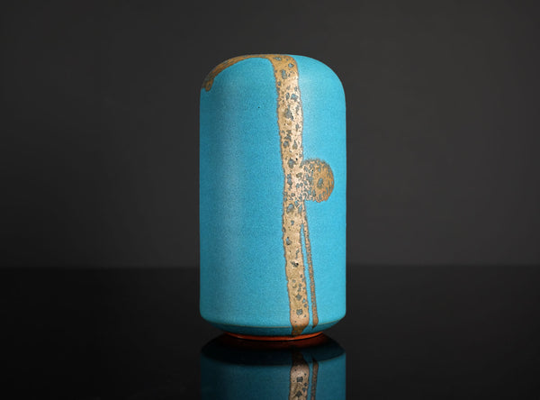 Blue cylindrical ceramic vase with gold accents on a dark background