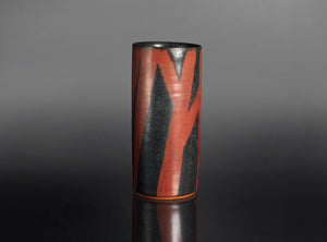 Cylindrical vase with red and black abstract design on a gray background
