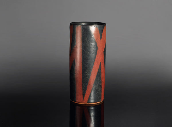 Cylindrical vase with black and red design on a gray background